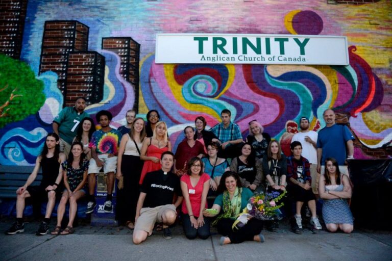 Group photo in front of the colorful mural at Trinity United Church, featuring diverse individuals celebrating community and togetherness.