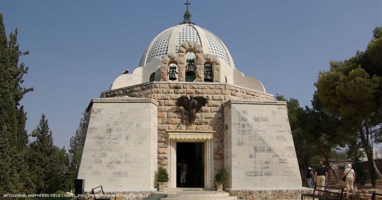 A stone building with a prominent dome and cross on top, featuring an eagle emblem above the entrance, set against a clear blue sky.
