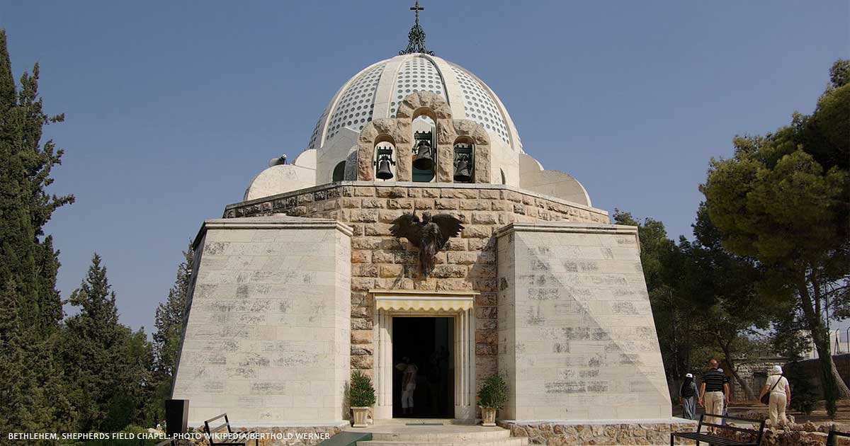 A stone building with a prominent dome and cross on top, featuring an eagle emblem above the entrance, set against a clear blue sky.