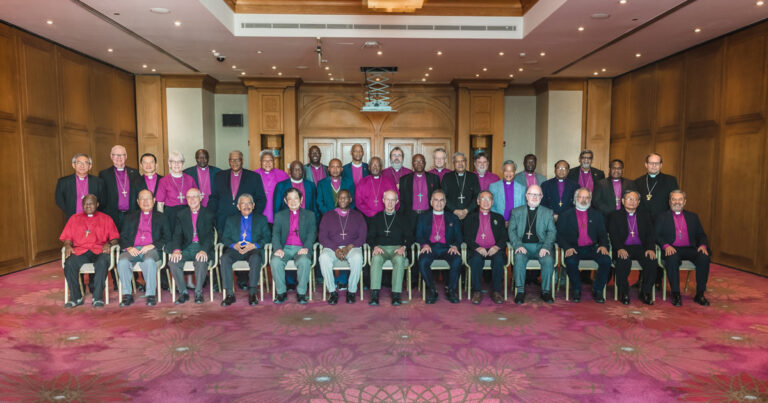 Group photo of a diverse assembly of individuals dressed in formal attire, seated and standing in a hotel conference room, with a focus on unity and collaboration.