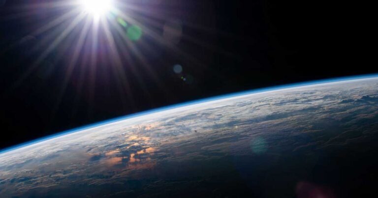 A view of Earth from space, showcasing the curvature of the planet and the sun's rays illuminating the atmosphere.