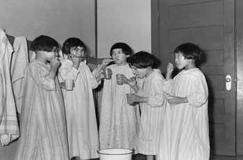 (Left to right) Connie Cox (née Pachano), Elsie Pepabano, Juliet Bearskin (née Head), Annie Jolly (née Tapiatit) and Maria Fleming brush their teeth at bedtime (1947-1948). ANGLICAN CHURCH OF CANADA GENERAL SYNOD ARCHIVES