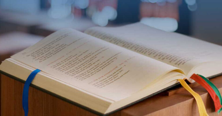 Open book with visible text pages, resting on a wooden surface, with blurred background lights.