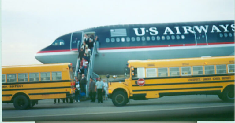 Passengers disembarking from a U.S. Airways airplane onto a tarmac, with yellow school buses waiting nearby for transportation.