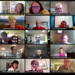 A virtual meeting with multiple participants displayed in a grid format, featuring individuals engaged in discussion. Some participants are focused on their screens, while others appear to be speaking or listening attentively. The background includes various home office settings.