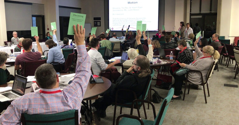 Audience members raising green cards during an interactive session at a conference, with a presentation screen visible in the background.