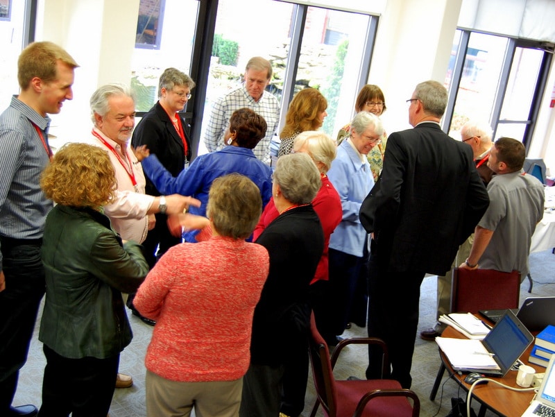A group of people engaged in conversation during a community event, with a mix of ages and attire, gathered in a brightly lit room.
