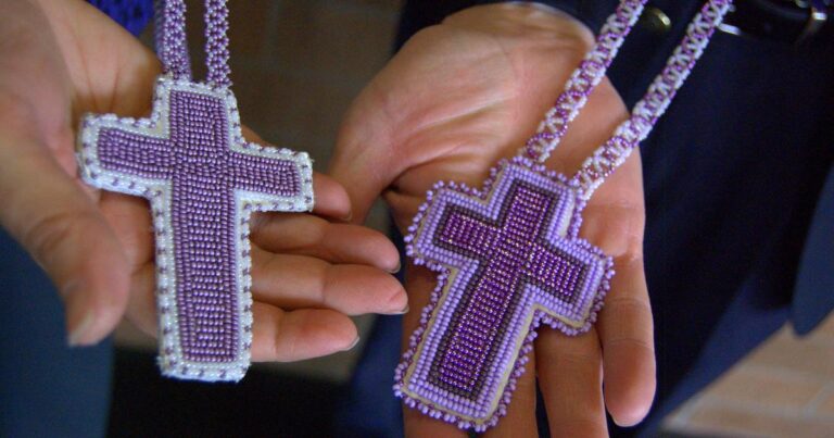 Two intricately beaded purple cross necklaces held in hands, showcasing detailed craftsmanship and design.