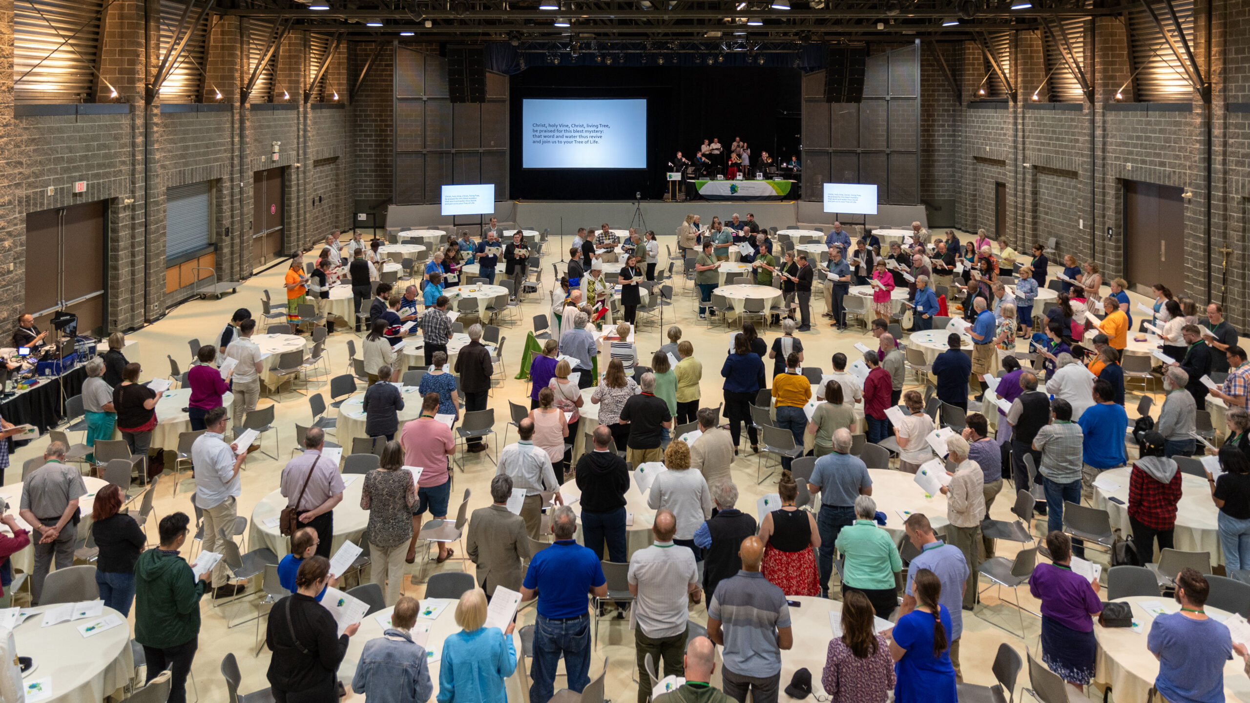 crowd of delegates standing infant of a projector screen at the opening worship in Calgary, Alberta.