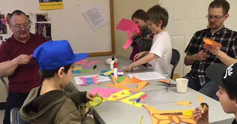 Children engaged in a creative craft activity, using colorful paper and glue to make art projects at a table.