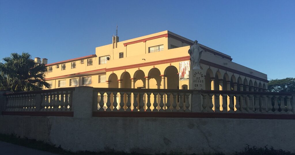 Historic building with arched porch and decorative columns, bathed in warm sunlight against a clear blue sky.