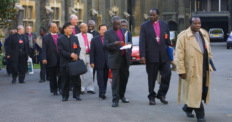 Group of bishops in formal attire walking together outside a church, engaged in conversation and holding documents. The setting appears to be a religious or ceremonial event.