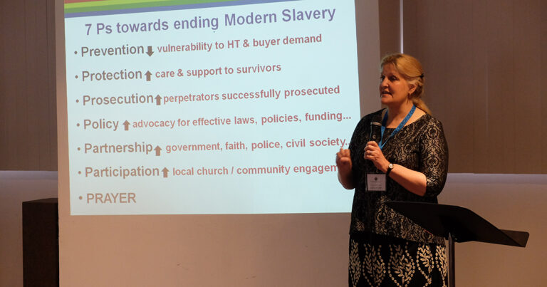 A speaker presenting strategies for ending modern slavery, with a slide displaying key points on vulnerability, support for survivors, and collaboration among various sectors.