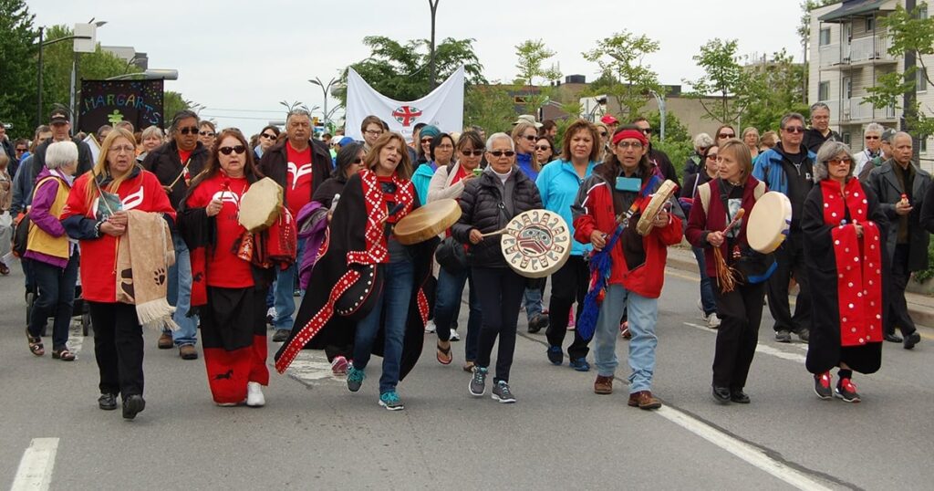Participants in traditional attire march in a cultural parade, holding drums and banners, celebrating community heritage and unity.