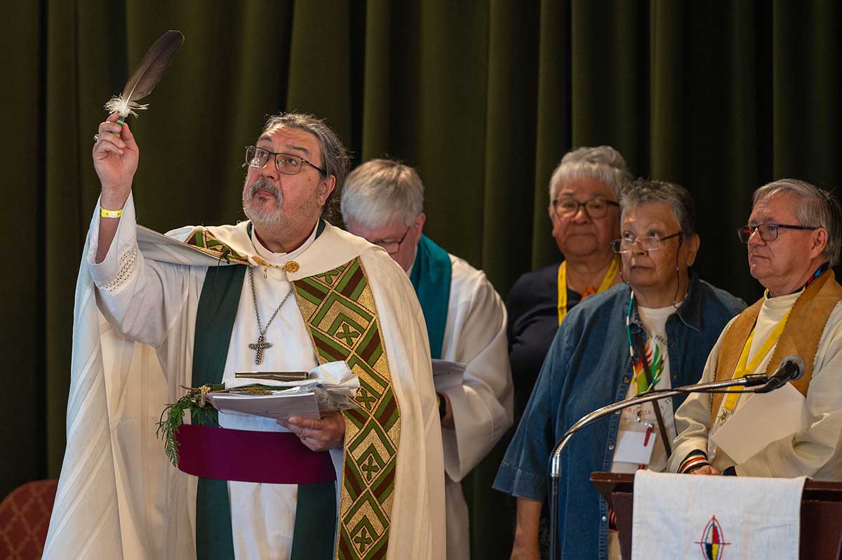 Archbishop Chris Harper holding up an eagle feather while other people look on.