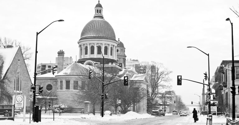 Historic building with a large dome covered in snow, surrounded by a winter landscape and traffic lights.