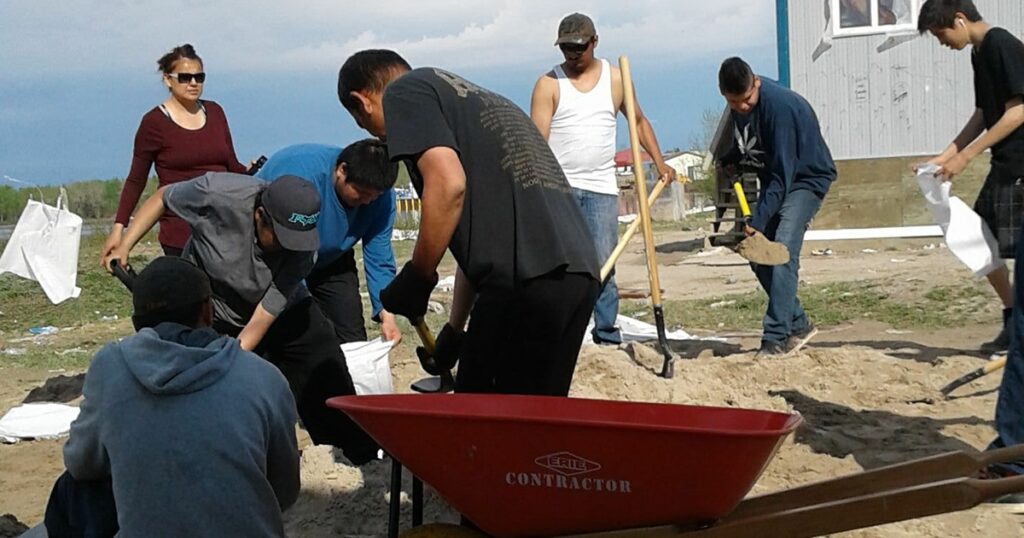 Group of people working together in a garden, using shovels and a wheelbarrow to prepare the soil for planting.