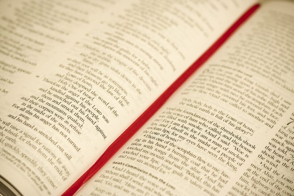 Close-up of open Bible showing spread of two pages, with red ribbon between them.