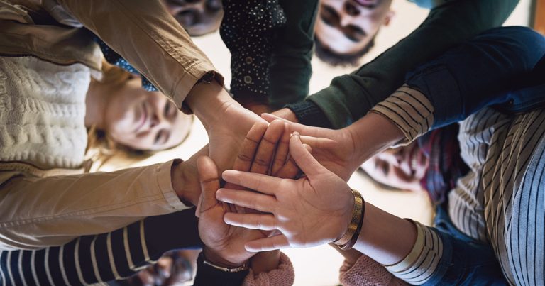 Seen from below, a smiling group of young adults join hands in the centre of a circle.