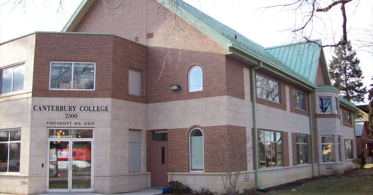 Brick building with a green roof labeled "College," featuring large windows and a welcoming entrance, surrounded by a landscaped area.