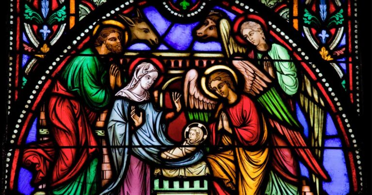 Stained glass window depicting the Nativity scene, featuring Mary, Joseph, an angel, and baby Jesus, surrounded by animals and vibrant colors.