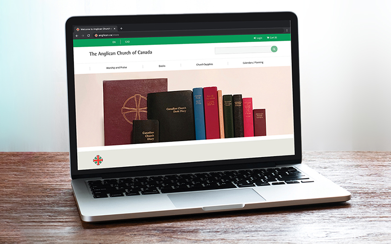 Laptop displaying the website of The Anglican Church of Canada, featuring a collection of colorful books on a wooden surface.