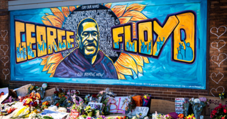 Mural depicting George Floyd with the words "FREE FLOYD" surrounded by vibrant colors and sunflowers, alongside a memorial of flowers and messages at the base.