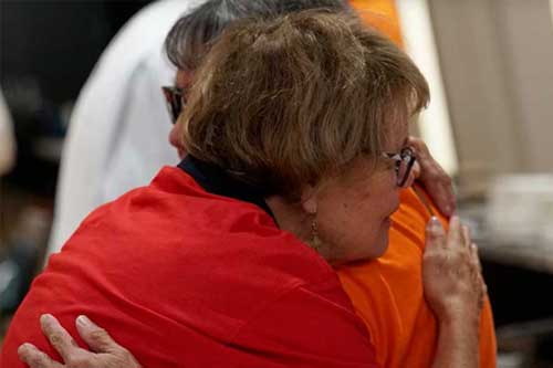 Two people embrace in a warm hug, wearing red and orange shirts.