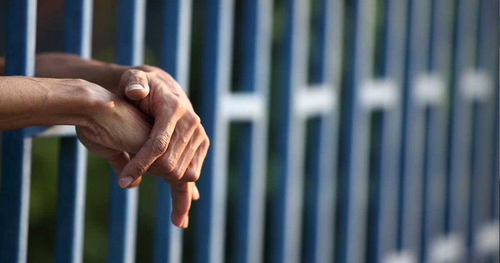 Hands in a jailcell. Photo: Shutterstock.
