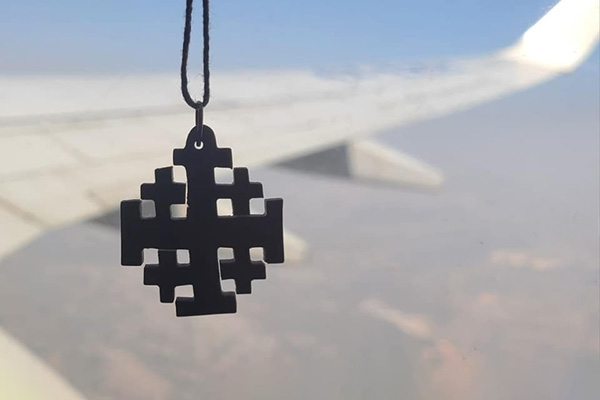 Silhouette of wooden Jerusalem cross against a background presumably looking out a plane window at the plane wing.