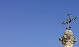 Stone church cross atop a column against a clear blue sky