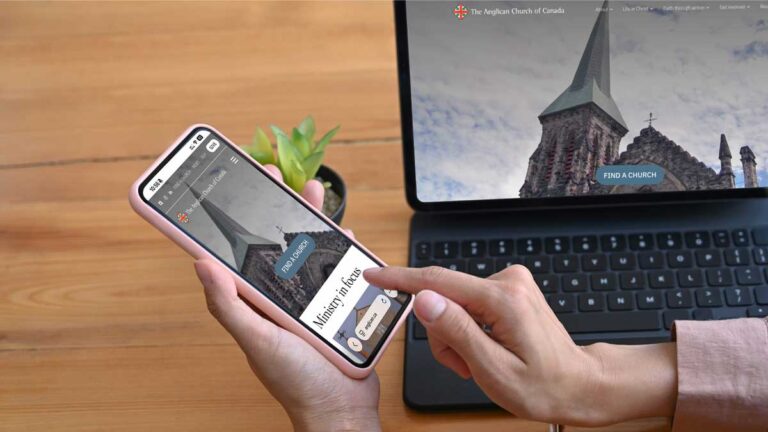A person using a smartphone to browse the Anglican Church of Canada’s new website, with the same church-steeple page open on a laptop in the background showing a “Find a Church” button.