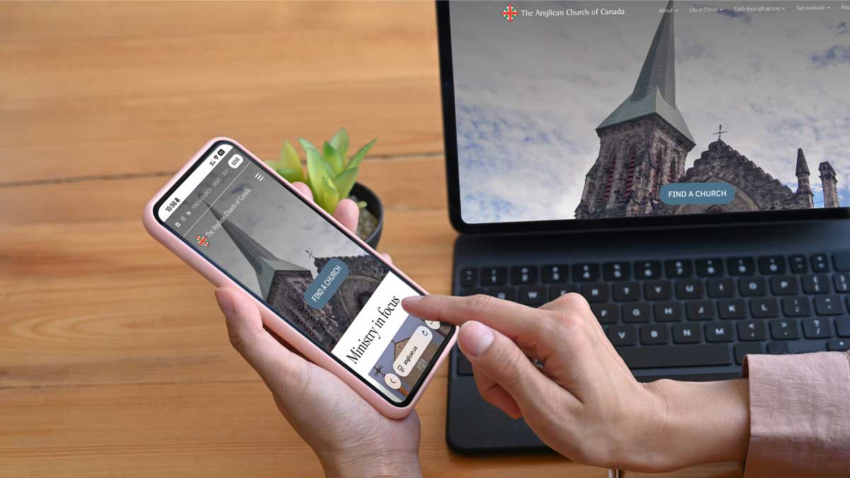 A person using a smartphone to browse the Anglican Church of Canada’s new website, with the same church-steeple page open on a laptop in the background showing a “Find a Church” button.