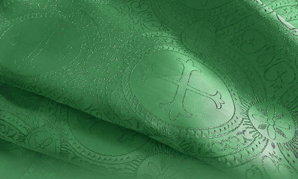 Close-up of green liturgical fabric with a woven cross pattern and ornamental brocade detail.