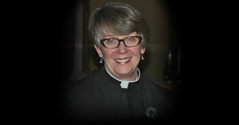 A smiling woman wearing glasses and a clerical collar, set against a dark background, representing a religious or spiritual context.