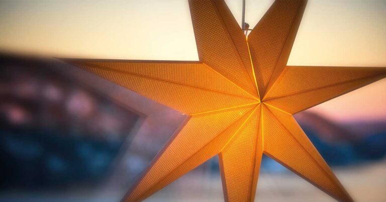 Orange paper star decoration hanging against a blurred background, symbolizing festive celebrations.