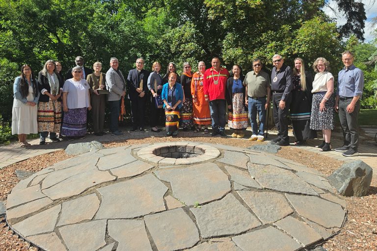 Representatives from the National Centre for Truth and Reconciliation, Anglican Church of Canada, United Church of Canada and Presbyterian Church in Canada stand together around a stone fire pit at the NCTR gifting ceremony in June 2026.