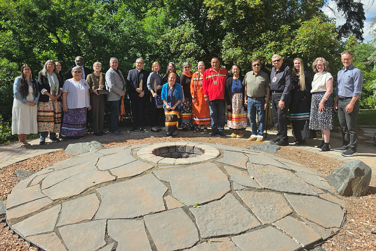 Representatives from the National Centre for Truth and Reconciliation, Anglican Church of Canada, United Church of Canada and Presbyterian Church in Canada stand together around a stone fire pit at the NCTR gifting ceremony in June 2026.