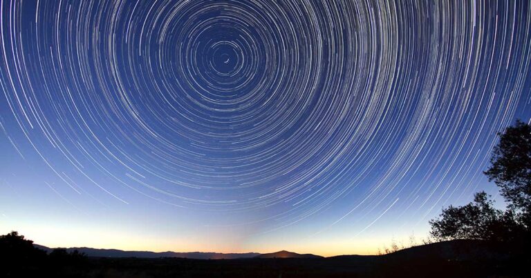 Star trails forming circular patterns in the night sky above a horizon, showcasing the movement of stars over time.