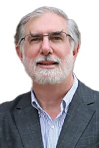 Archdeacon Allan Perry wearing glasses, a grey blazer, and a light blue collared shirt, facing the camera against a white background.