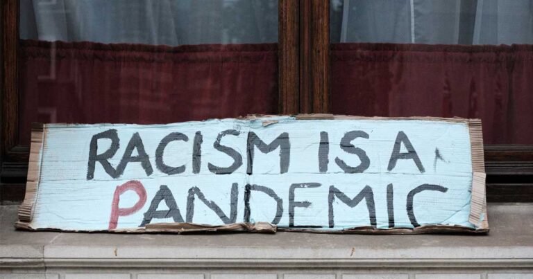 A sign displayed in a window reads "Racism is a Pandemic," emphasizing a social message about the impact of racism.