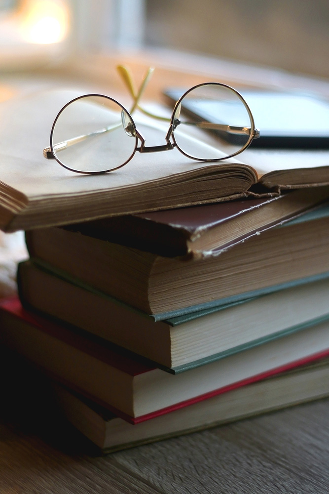 E-book device and glasses set on top of a stack of printed books