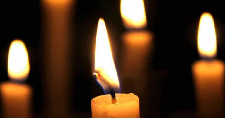 A close-up of a lit candle with a bright flame against a dark background, creating a warm and serene atmosphere.