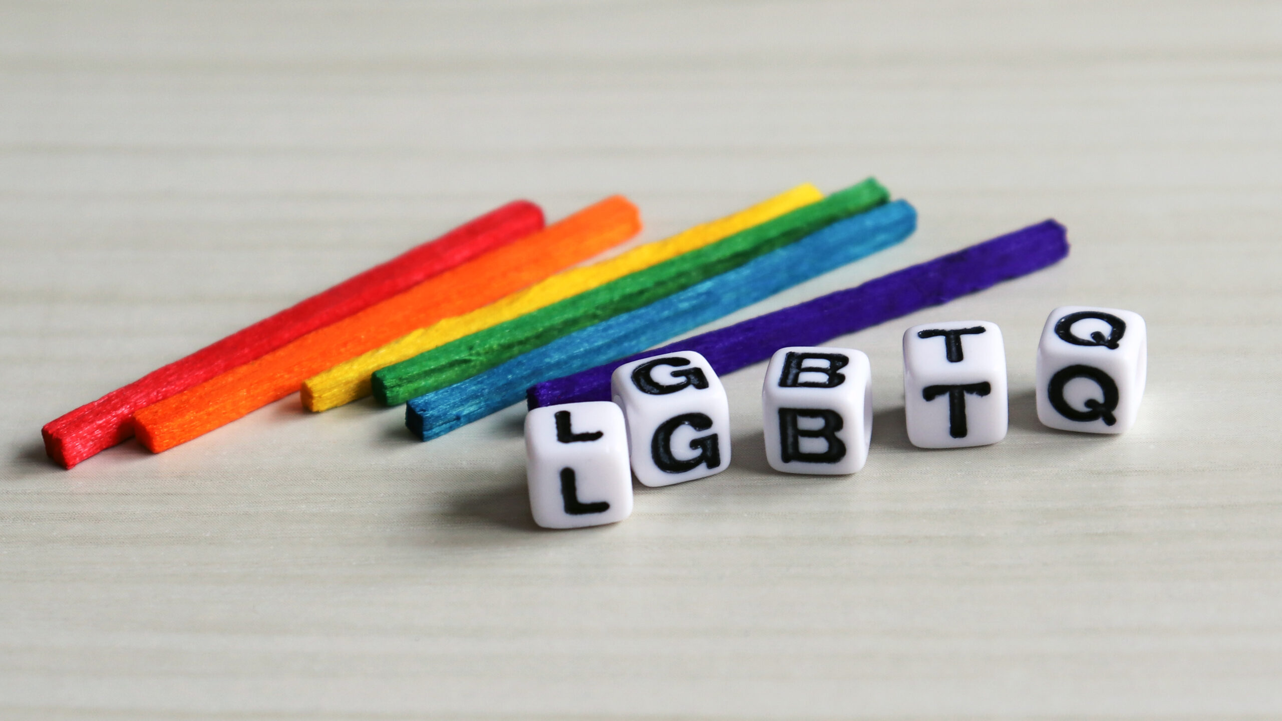 Colorful craft sticks arranged in a row with white letter beads spelling "LGBT" positioned below them, symbolizing support for the LGBTQ+ community.