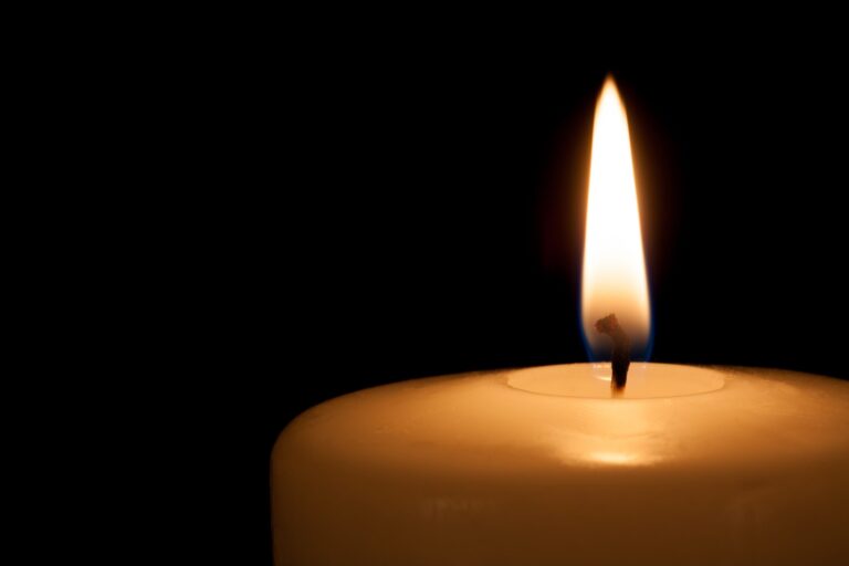 A close-up of a lit candle against a dark background, showcasing the flickering flame and the smooth surface of the candle.