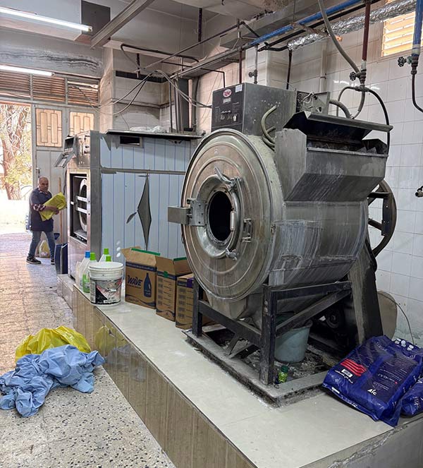 Industrial laundry room with large washing machines, supplies, and a worker handling linens.