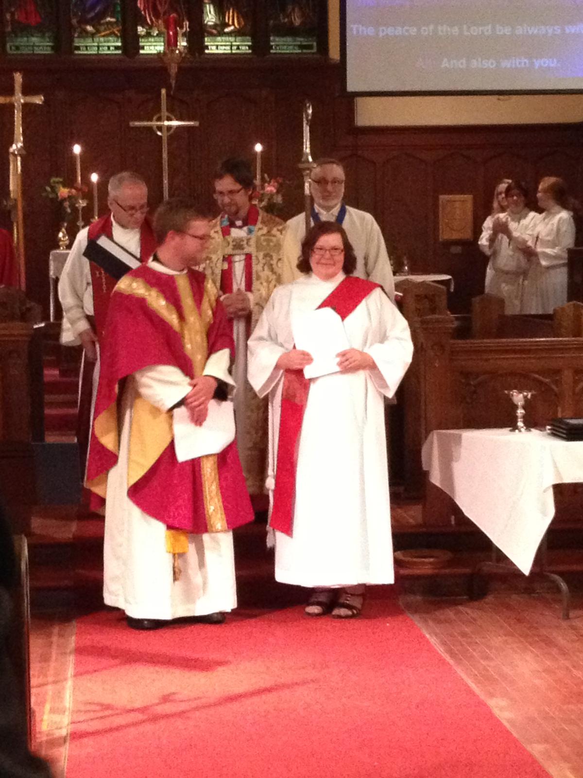 Clergy members in religious attire participating in a ceremonial event in a church setting, with a congregation in the background.