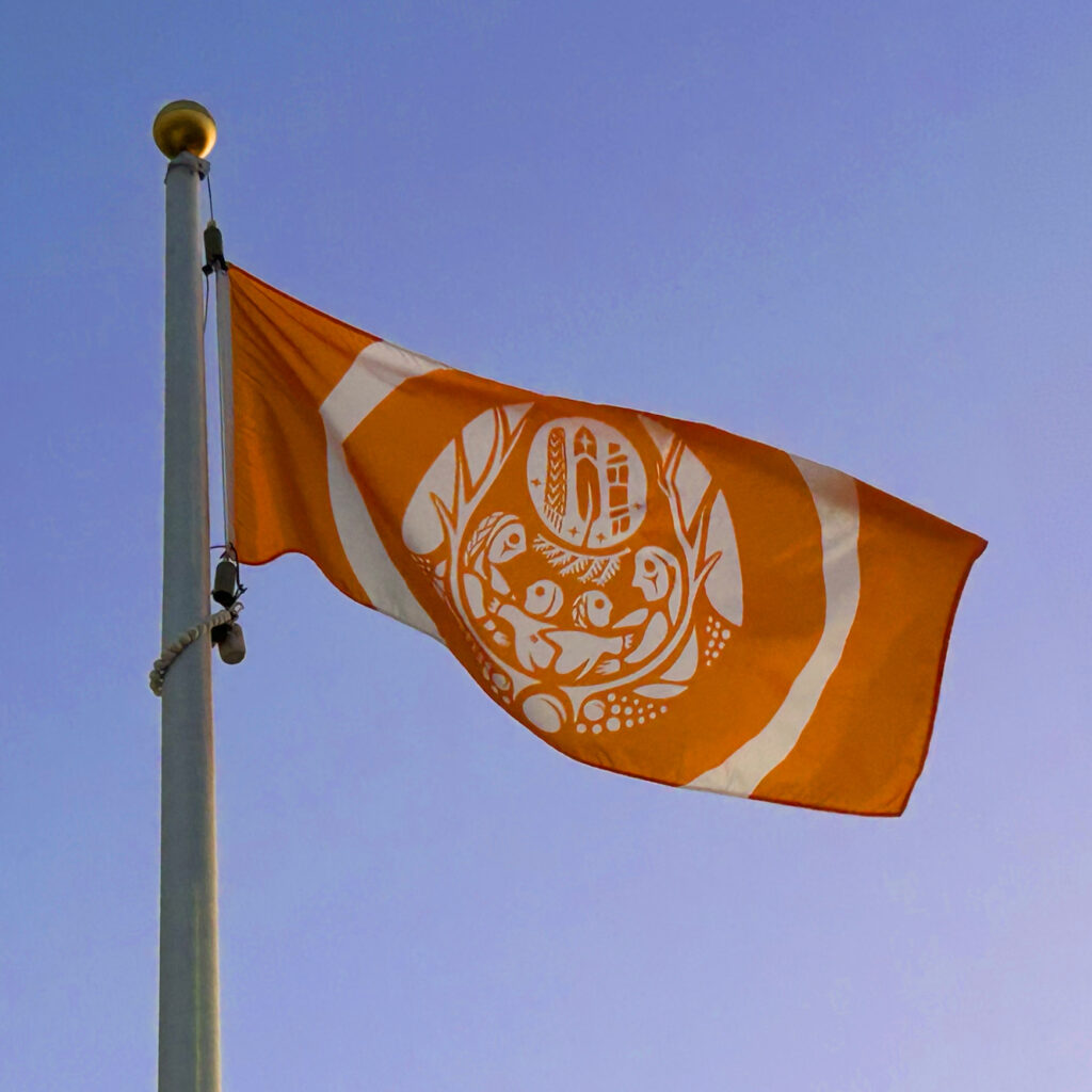 Orange and white Survivors' Flag flying on a flagpole against a clear blue sky